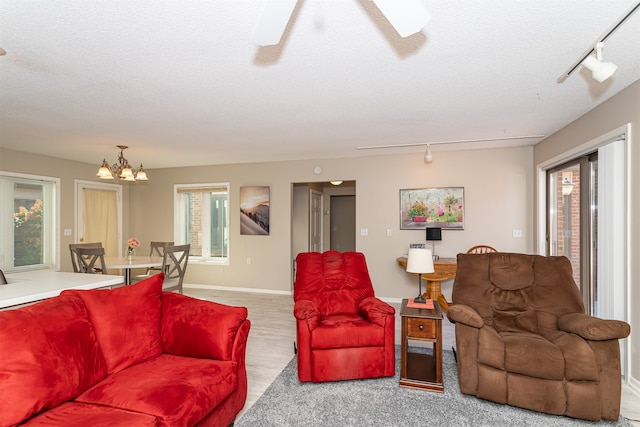 carpeted living room featuring ceiling fan with notable chandelier, a textured ceiling, and track lighting