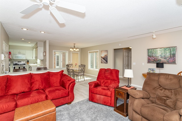 living room with ceiling fan with notable chandelier, light wood-type flooring, a textured ceiling, and sink