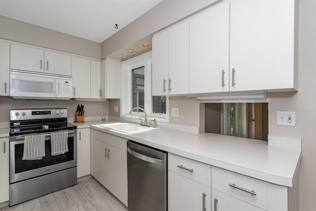 kitchen with white cabinets, sink, a textured ceiling, light hardwood / wood-style flooring, and appliances with stainless steel finishes