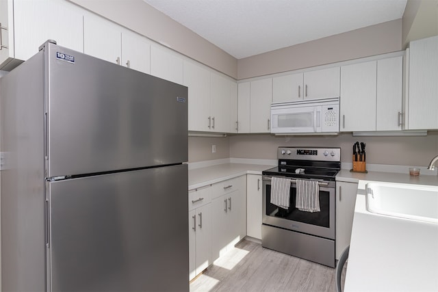 kitchen with light wood-type flooring, a textured ceiling, stainless steel appliances, and white cabinets