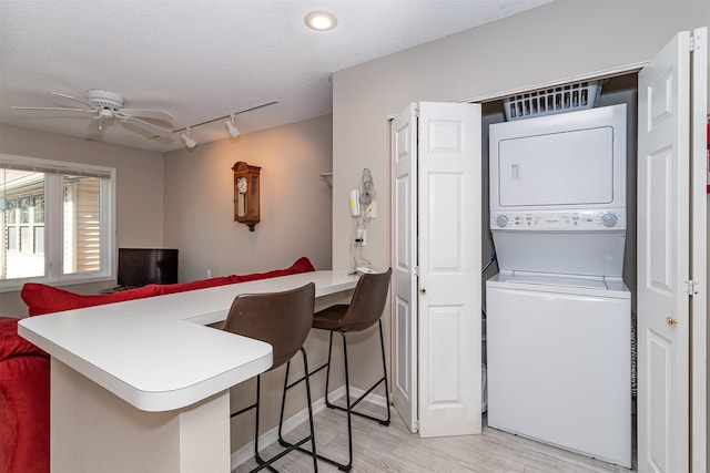 kitchen with stacked washer and clothes dryer, kitchen peninsula, a breakfast bar area, and ceiling fan