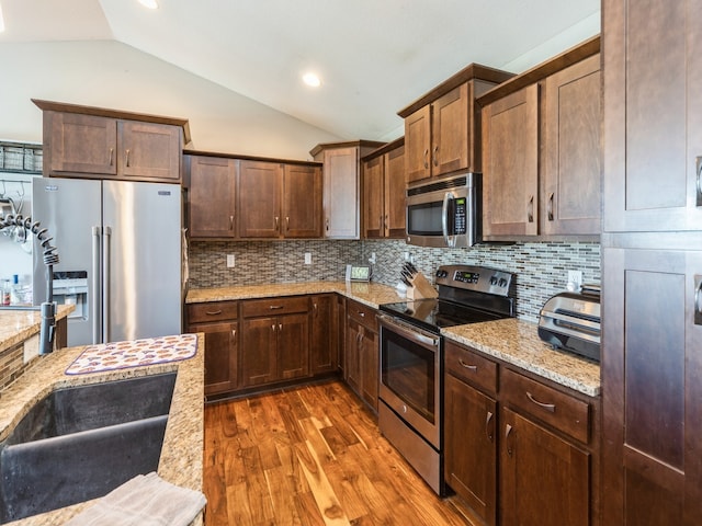 kitchen featuring light stone counters, appliances with stainless steel finishes, and vaulted ceiling