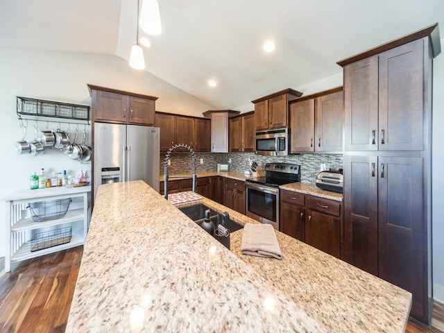 kitchen with light stone countertops, stainless steel appliances, vaulted ceiling, sink, and pendant lighting