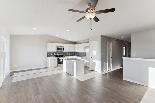 kitchen featuring ceiling fan, appliances with stainless steel finishes, a kitchen island with sink, vaulted ceiling, and white cabinets