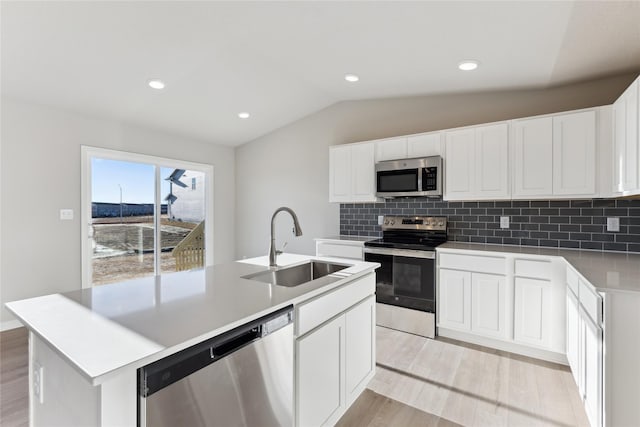 kitchen with appliances with stainless steel finishes, a kitchen island with sink, vaulted ceiling, white cabinets, and sink