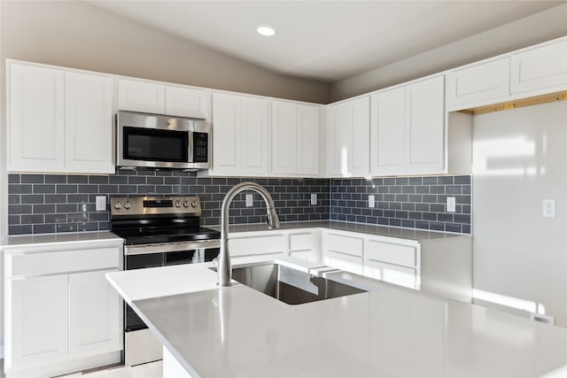 kitchen featuring backsplash, sink, white cabinetry, an island with sink, and stainless steel appliances