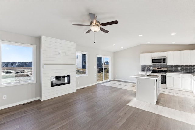 kitchen with lofted ceiling, a center island with sink, decorative backsplash, appliances with stainless steel finishes, and white cabinets