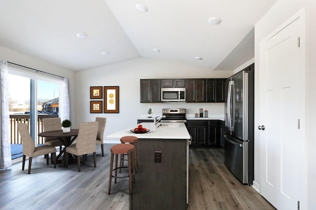 kitchen featuring appliances with stainless steel finishes, vaulted ceiling, dark wood-type flooring, a breakfast bar area, and an island with sink