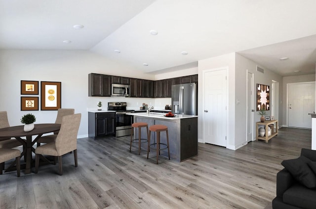 kitchen featuring dark brown cabinetry, stainless steel appliances, a center island with sink, light hardwood / wood-style flooring, and a breakfast bar area