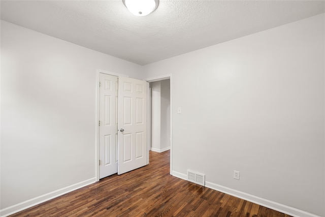 spare room featuring a textured ceiling and dark hardwood / wood-style flooring