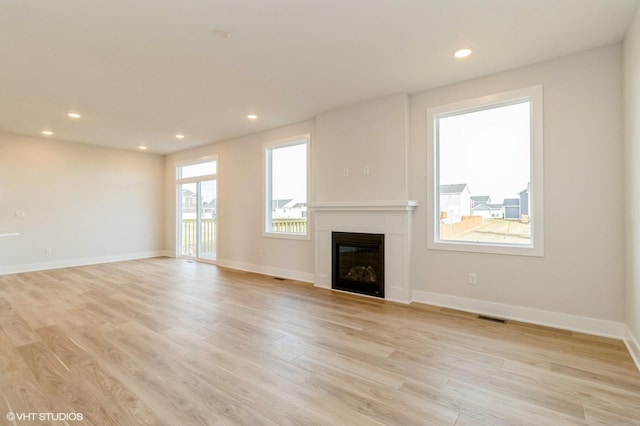 unfurnished living room with recessed lighting, visible vents, baseboards, light wood-style floors, and a glass covered fireplace