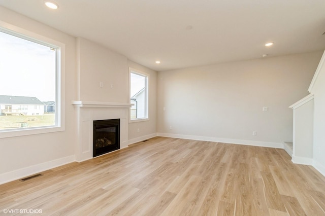 unfurnished living room with recessed lighting, visible vents, baseboards, light wood finished floors, and a glass covered fireplace