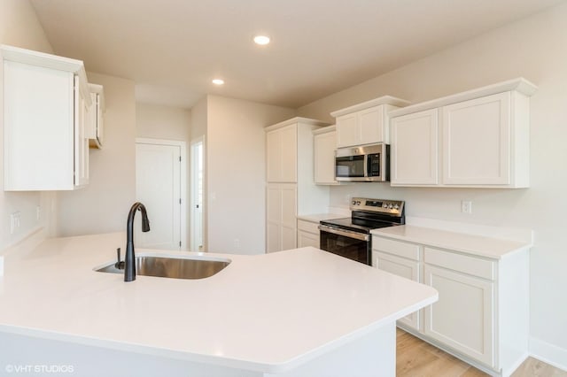 kitchen with recessed lighting, a peninsula, stainless steel appliances, white cabinetry, and a sink