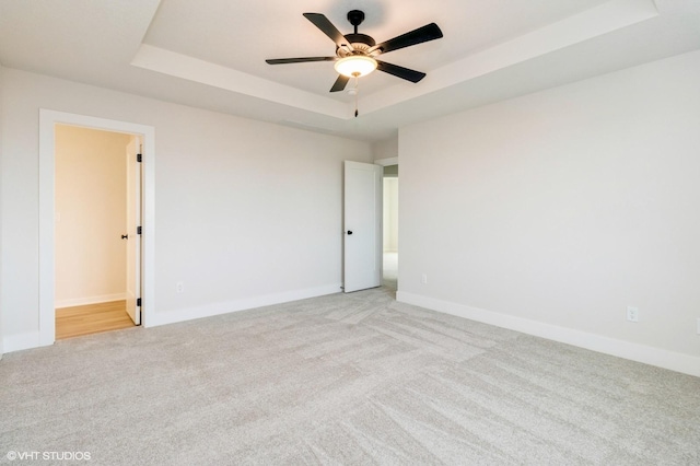 empty room featuring a raised ceiling, a ceiling fan, baseboards, and light carpet