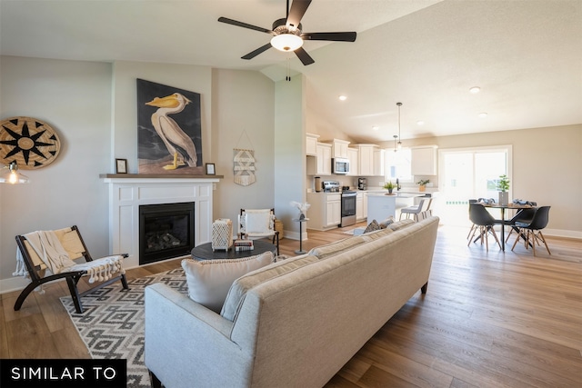 living room featuring ceiling fan, lofted ceiling, and light hardwood / wood-style flooring