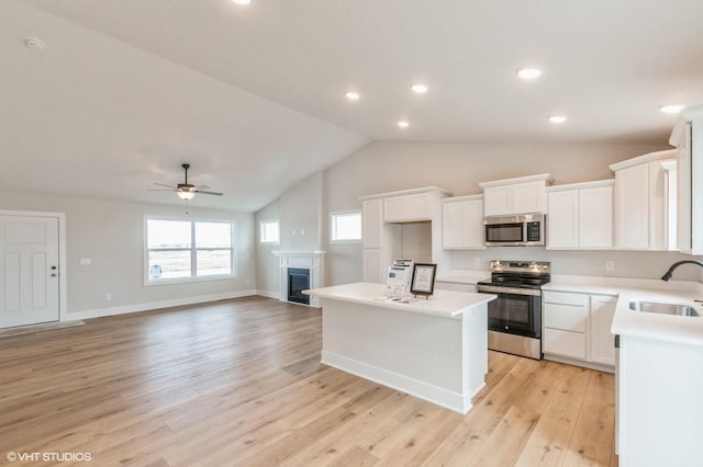 kitchen with stainless steel appliances, a kitchen island, a sink, white cabinets, and light countertops