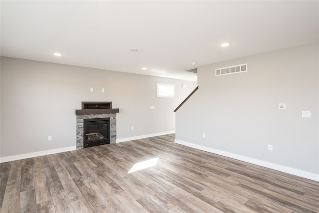 unfurnished living room featuring a stone fireplace and light wood-type flooring