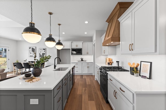 kitchen with a large island with sink, white cabinetry, hanging light fixtures, and black appliances