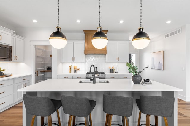 kitchen with white cabinets, sink, a kitchen island with sink, and black microwave