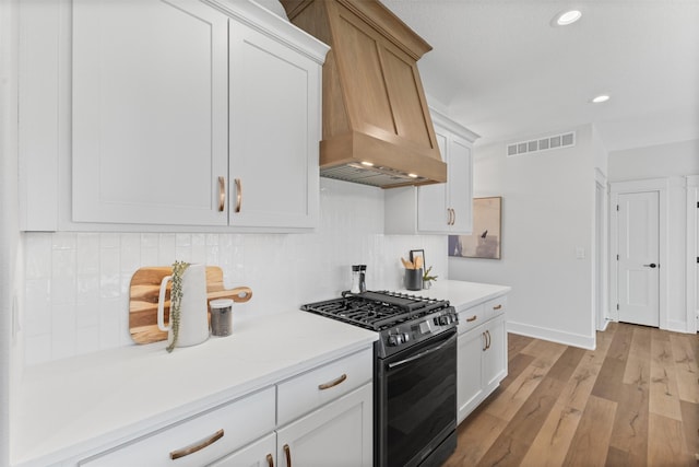 kitchen featuring custom exhaust hood, black range with gas stovetop, decorative backsplash, light wood-type flooring, and white cabinetry