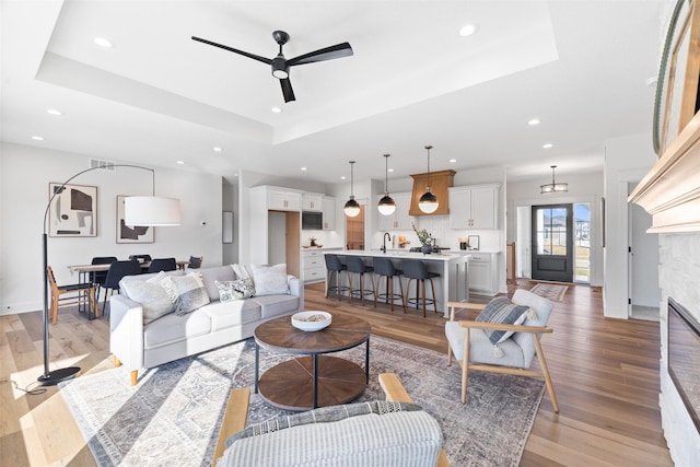 living room with ceiling fan, sink, a raised ceiling, light hardwood / wood-style floors, and a fireplace