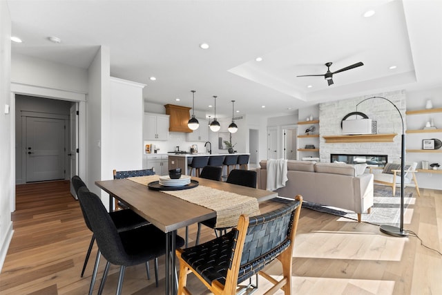 dining space with a raised ceiling, ceiling fan, a fireplace, and light hardwood / wood-style flooring