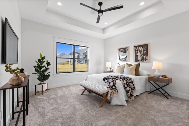 carpeted bedroom with ceiling fan and a tray ceiling