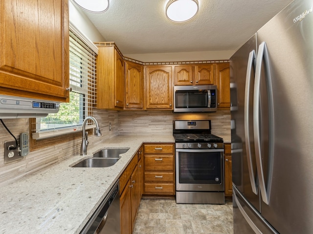 kitchen with tasteful backsplash, sink, stainless steel appliances, light stone countertops, and a textured ceiling