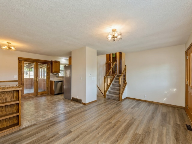 unfurnished living room featuring french doors, light hardwood / wood-style floors, and a textured ceiling