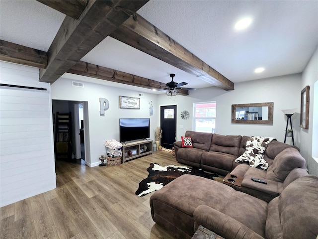 living room featuring ceiling fan, wood finished floors, visible vents, baseboards, and beamed ceiling