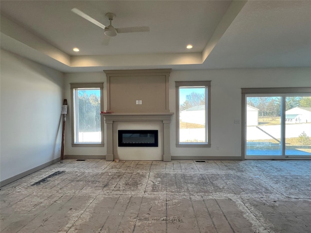 unfurnished living room featuring ceiling fan, a raised ceiling, and a wealth of natural light