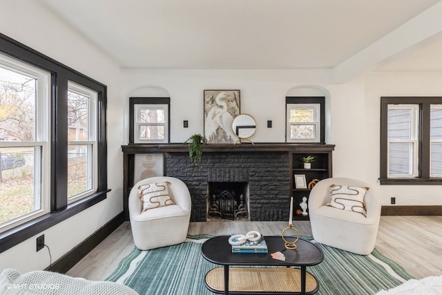 living room with a healthy amount of sunlight, wood-type flooring, and a brick fireplace