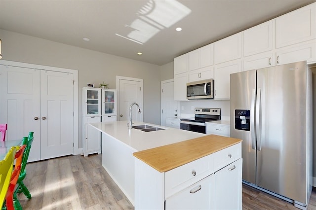 kitchen with light wood-type flooring, a center island with sink, sink, white cabinets, and appliances with stainless steel finishes