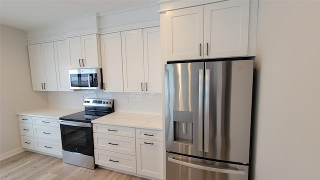 kitchen with light stone countertops, backsplash, appliances with stainless steel finishes, white cabinets, and light wood-type flooring