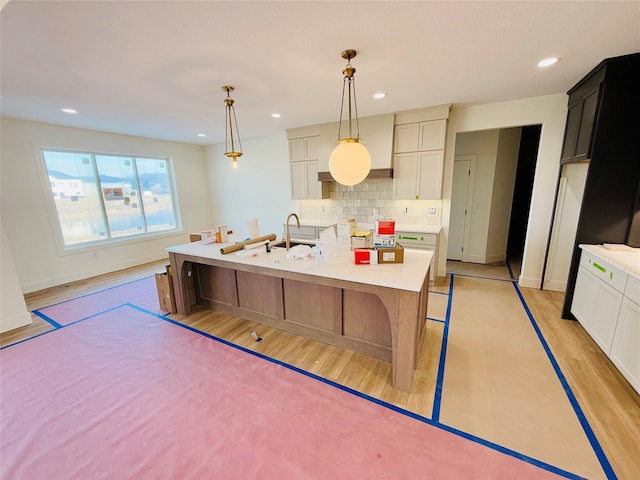 kitchen featuring an island with sink, light wood-type flooring, hanging light fixtures, sink, and decorative backsplash