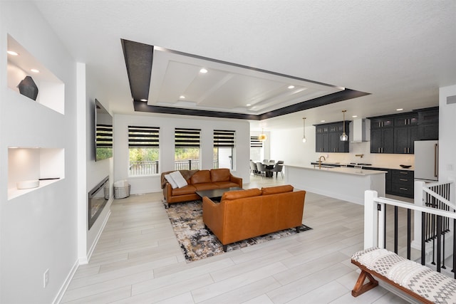 living room with a raised ceiling, light wood-type flooring, and a textured ceiling