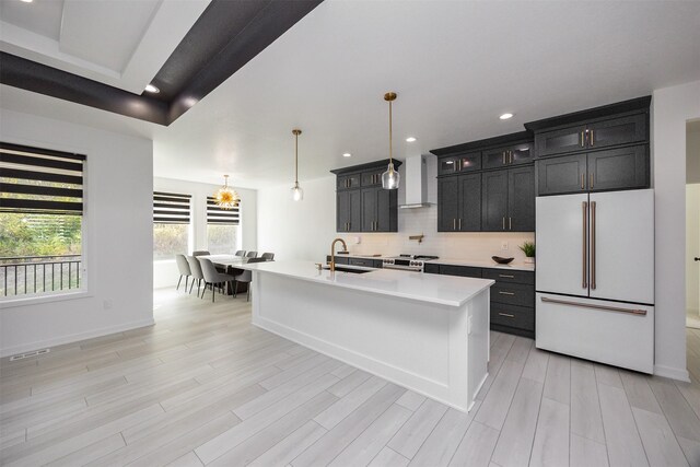 kitchen featuring wall chimney exhaust hood, pendant lighting, stainless steel range, a center island with sink, and white fridge