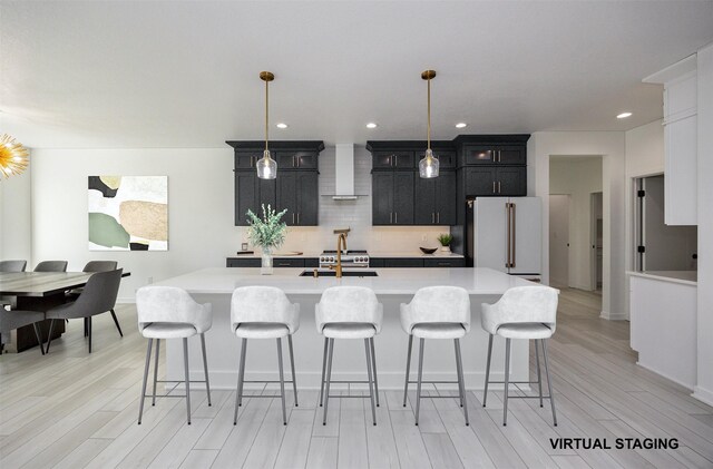 kitchen with pendant lighting, high end white refrigerator, a kitchen island with sink, and light hardwood / wood-style flooring