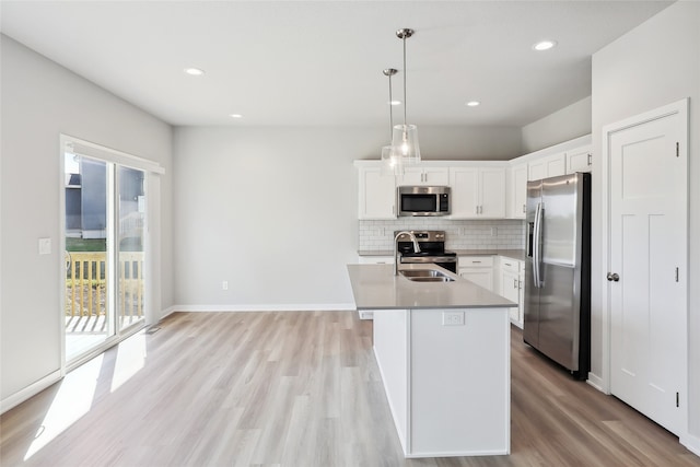 kitchen featuring light wood-type flooring, stainless steel appliances, hanging light fixtures, white cabinets, and an island with sink