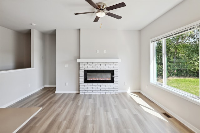 unfurnished living room featuring ceiling fan, a fireplace, a wealth of natural light, and light hardwood / wood-style flooring