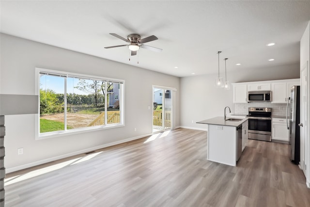 kitchen featuring a kitchen island with sink, stainless steel appliances, sink, hanging light fixtures, and white cabinetry