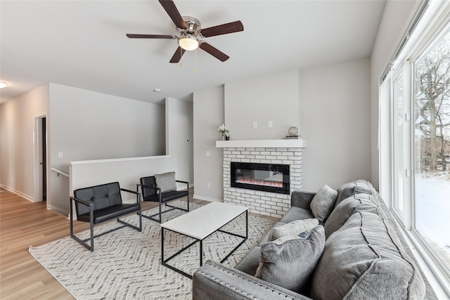 living room with a brick fireplace, ceiling fan, and light wood-type flooring