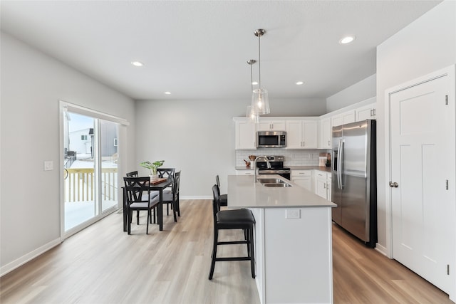 kitchen featuring white cabinetry, sink, hanging light fixtures, stainless steel appliances, and a center island with sink