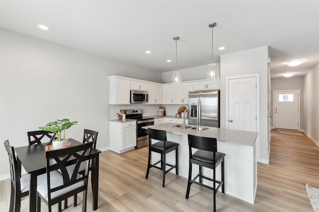 kitchen featuring sink, decorative light fixtures, stainless steel appliances, a kitchen island with sink, and white cabinets