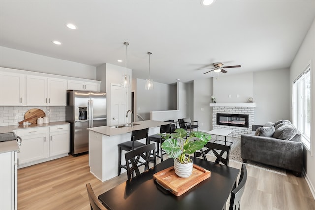 dining area with ceiling fan, light hardwood / wood-style floors, sink, and a brick fireplace