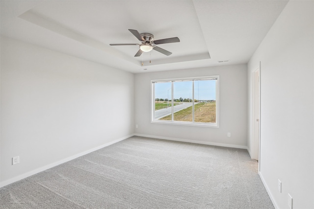 carpeted spare room with a tray ceiling and ceiling fan