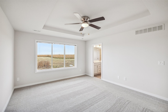 unfurnished room with ceiling fan, light colored carpet, and a raised ceiling