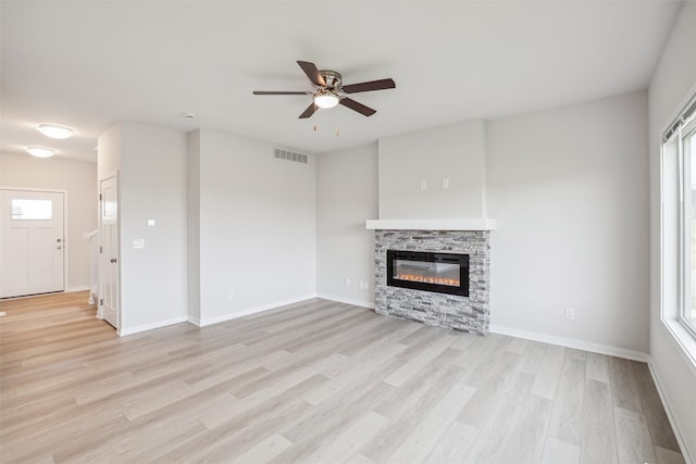 unfurnished living room with light hardwood / wood-style floors, a stone fireplace, and ceiling fan