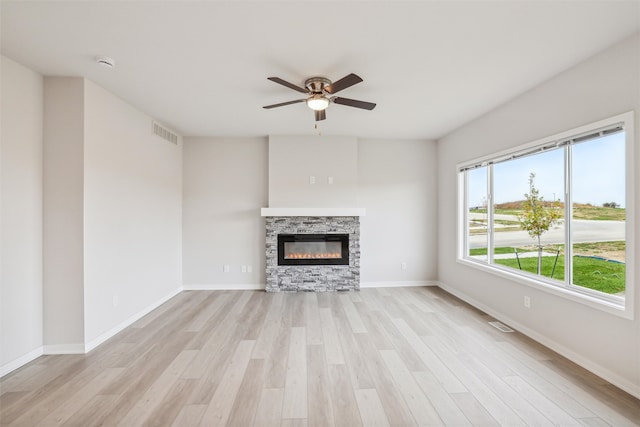 unfurnished living room featuring light hardwood / wood-style floors, a stone fireplace, and ceiling fan