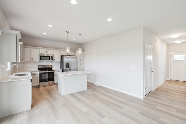 kitchen with appliances with stainless steel finishes, sink, a center island, light hardwood / wood-style floors, and pendant lighting